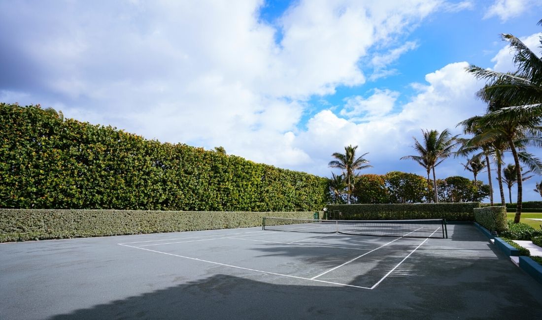 A variety of hedges and trees surround a Palm Beach tennis court maintained by Coastal Gardens.