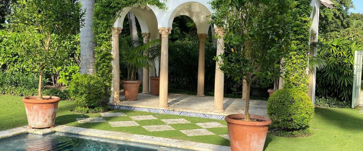 Terra cotta planters with trees flanking Mediterranean-style pool pavilion at luxury Palm Beach estate.