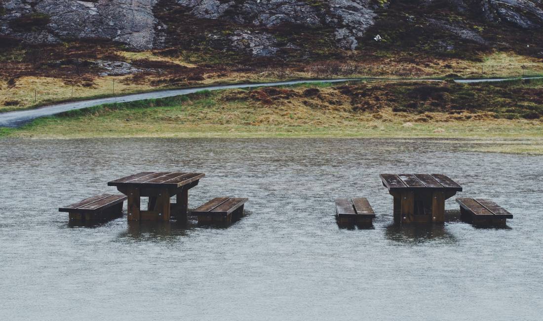 Two wooden picnic tables protrude from the surface of a flooded clearing.