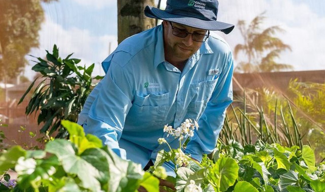 Estate gardener at Coastal Gardens carefully inspects blooming flowers, ensuring the health and upkeep of the entire coastal property landscape.
